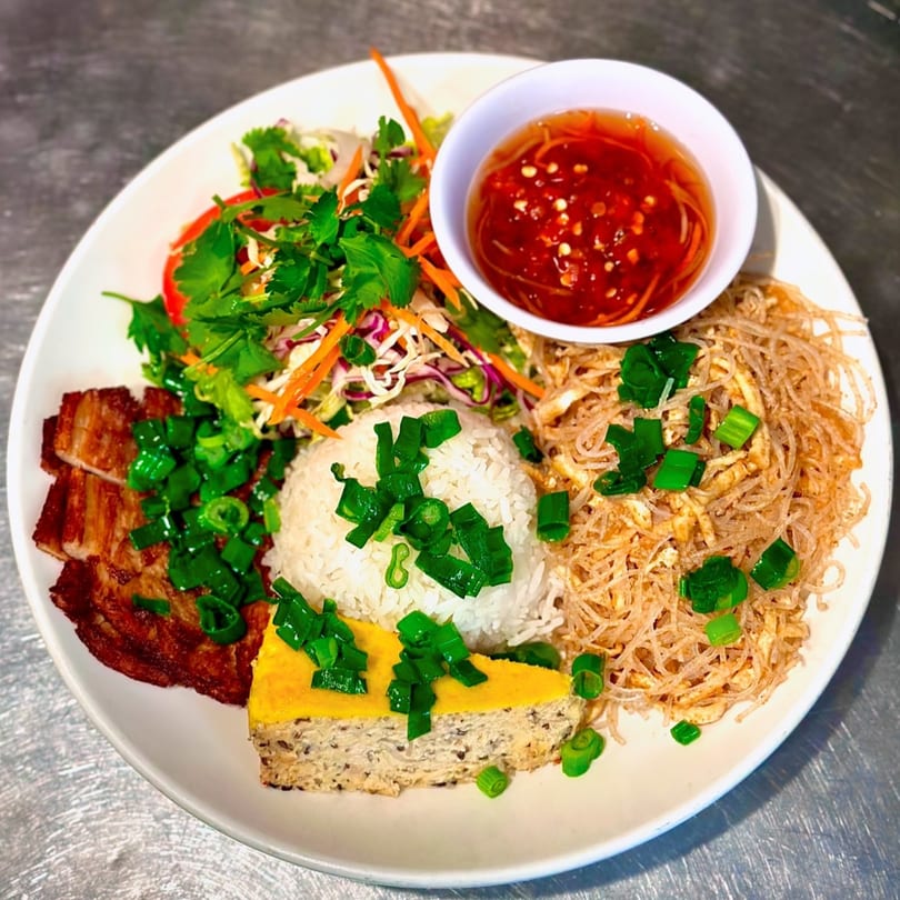 A vegan Vietnamese platter with rice, noodles, salad, sliced meat substitute, and a chili dipping sauce.