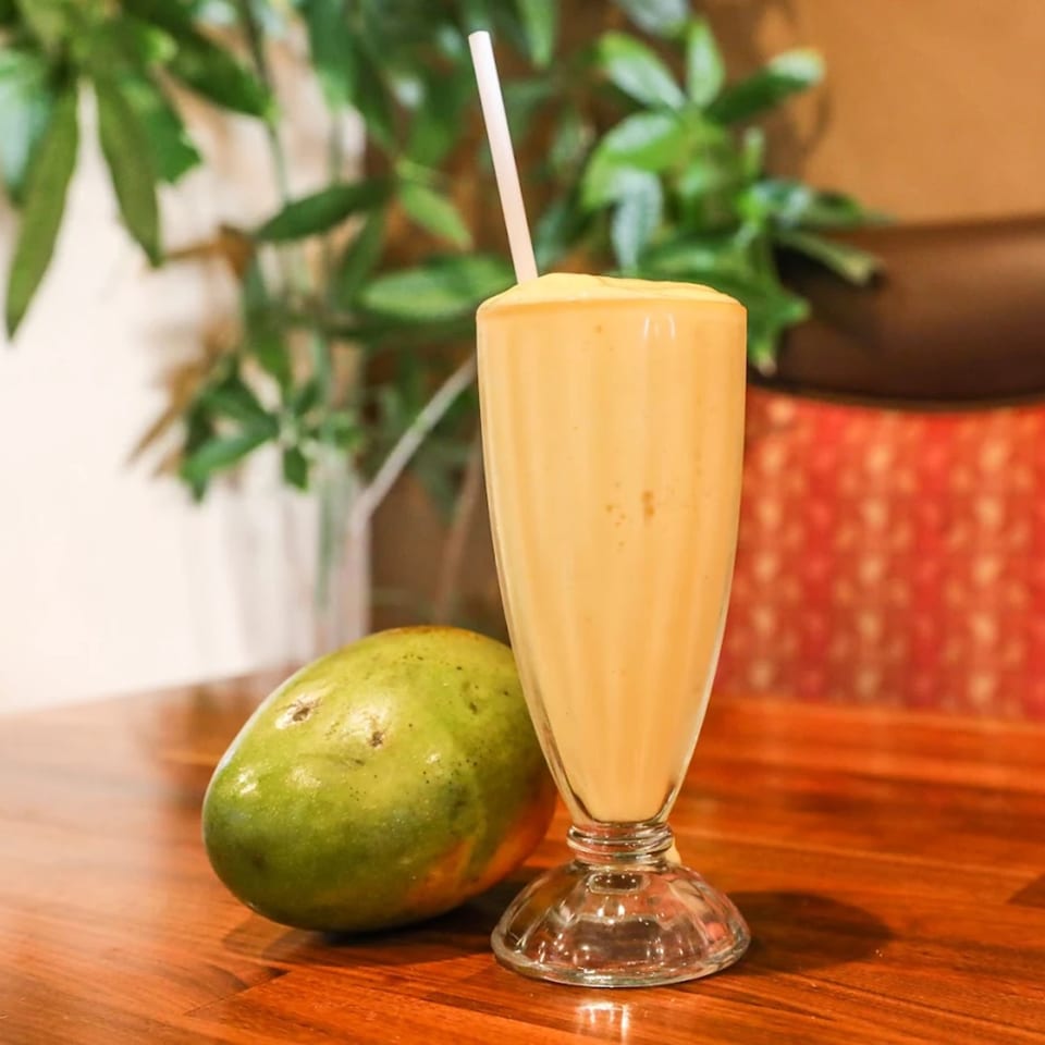 A tall glass of creamy mango lassi with a straw, next to a whole green mango.