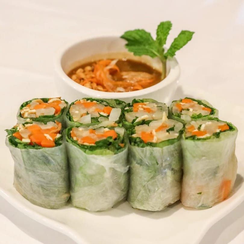 Eight vegan spring rolls with carrots, lettuce, and tofu, served with a peanut dipping sauce.