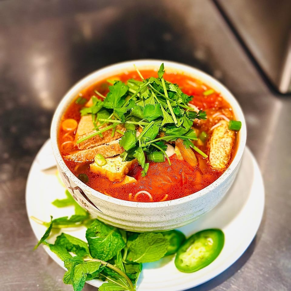 Vegan Bun Rieu soup with tofu, noodles, and herbs, served with mint and jalapeños.