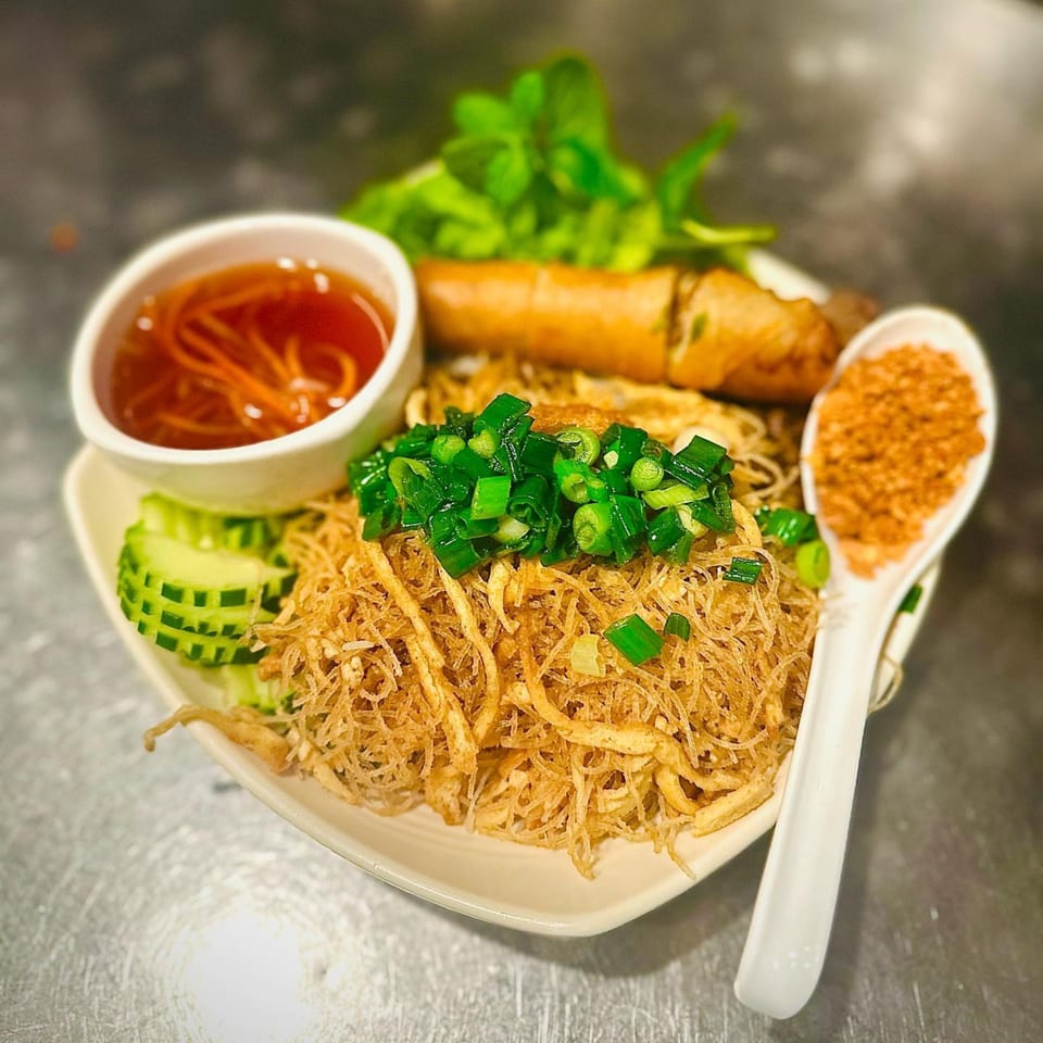 Vegan vermicelli noodles with a spring roll, fresh greens, cucumber, and dipping sauce.