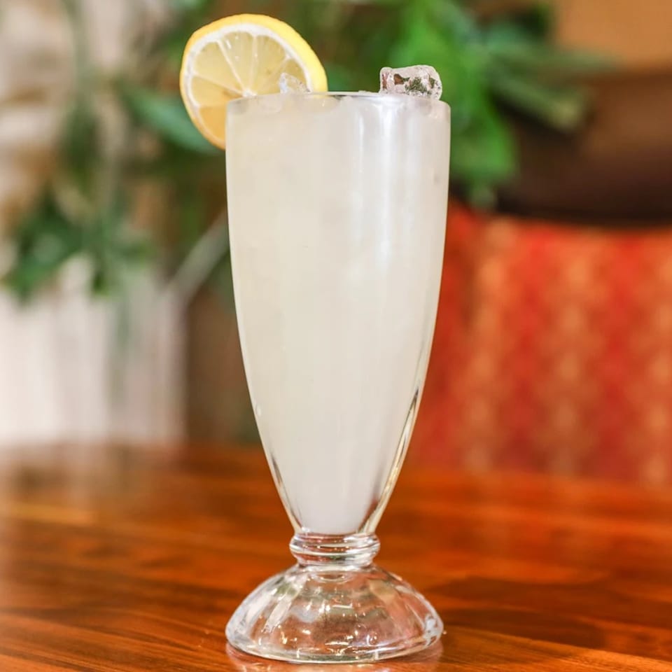 A tall glass of lemonade with ice and a lemon slice on a wooden table.