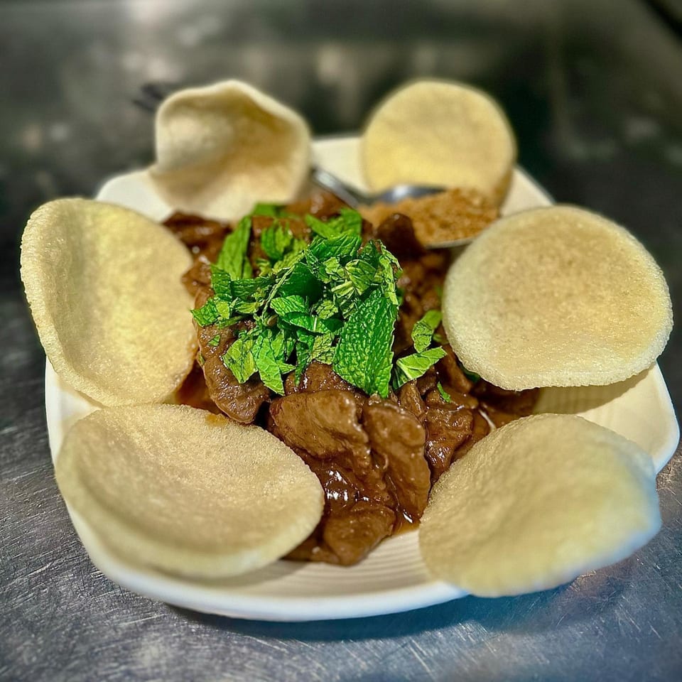Vegan beef and broccoli with mint garnish and crispy rice crackers on a white plate.