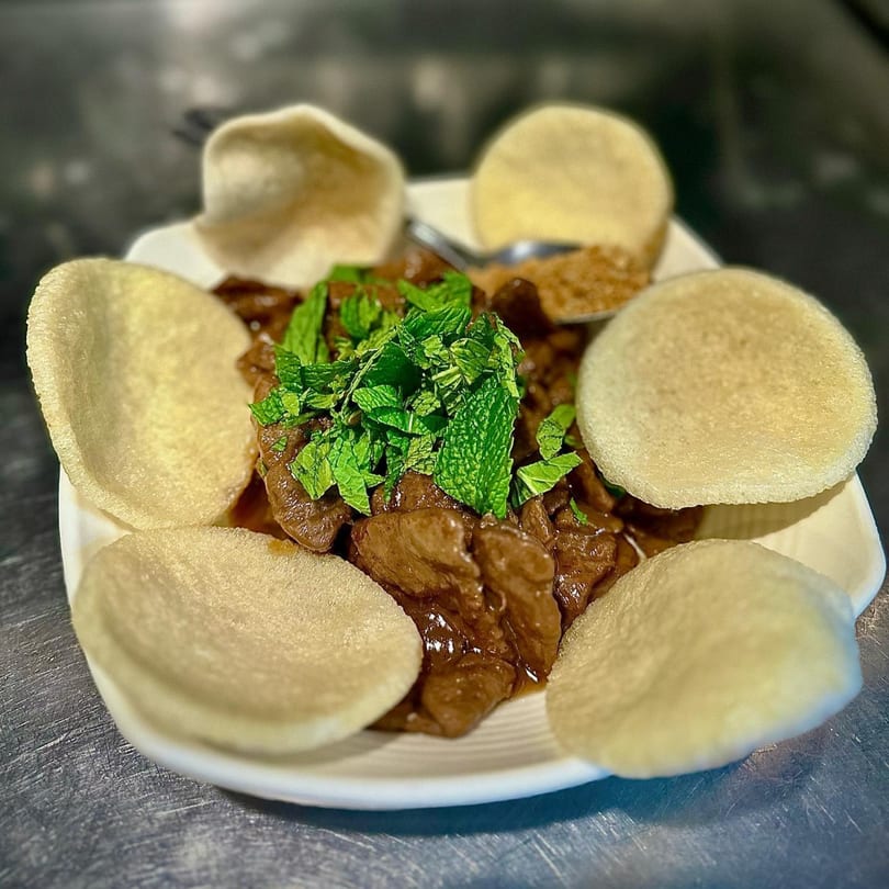 Vegan beef and broccoli with mint garnish and crispy rice crackers on a white plate.