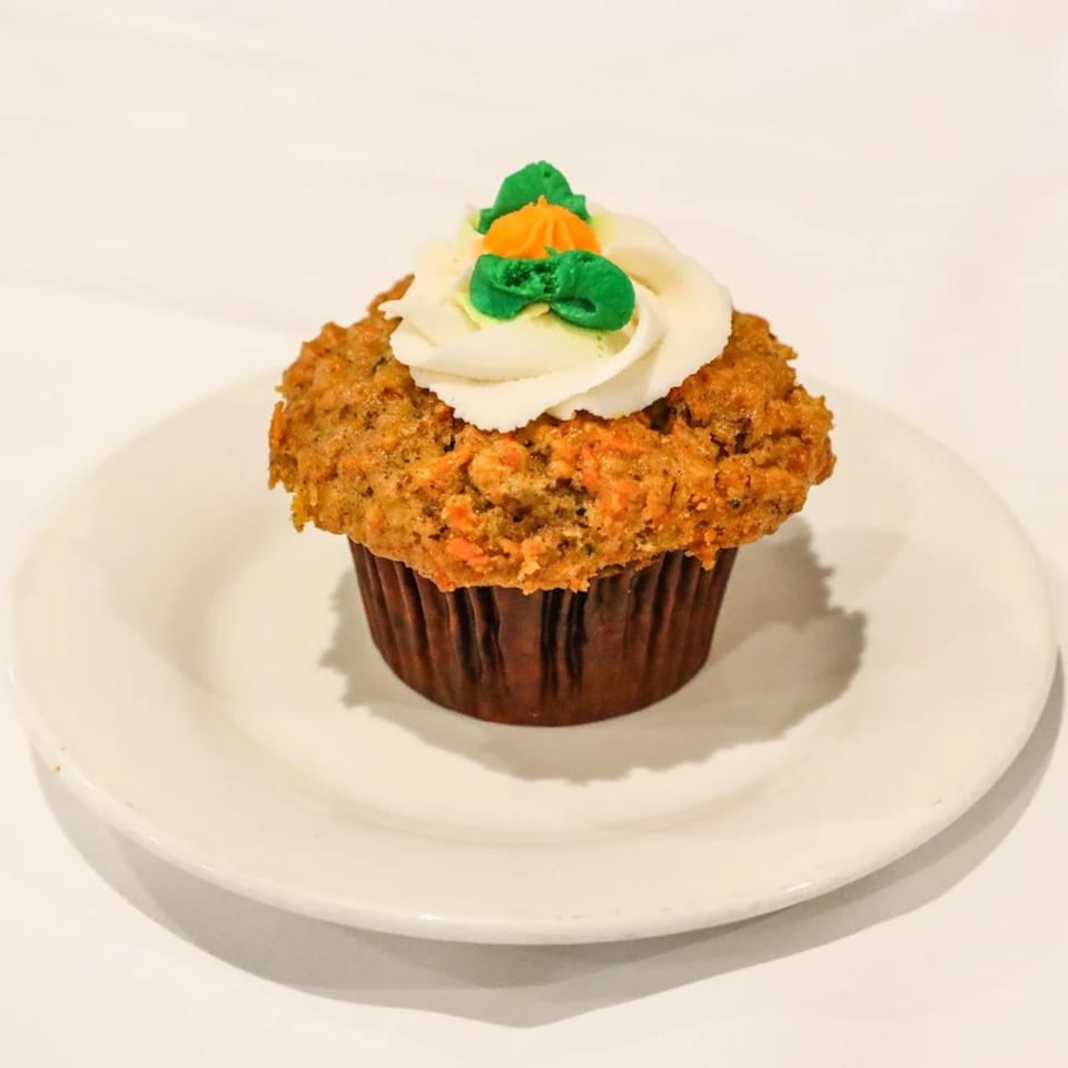 Vegan carrot cupcake with white frosting and green and orange carrot-shaped decorations on a white plate.