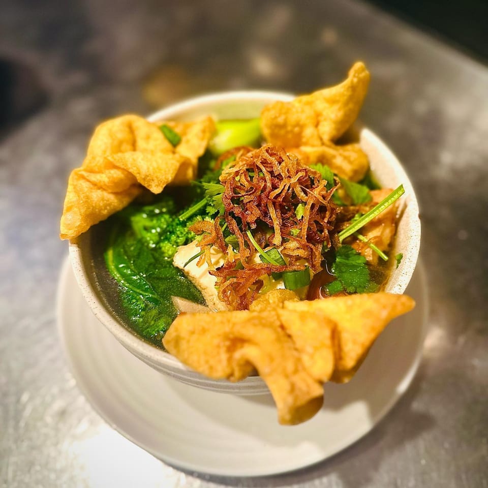 Vegan soup with tofu, green vegetables, fried onions, and crispy wontons in a white bowl.