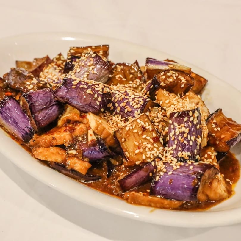 Blossom Vegan's eggplant dish with purple and brown pieces, coated in sauce and sesame seeds.