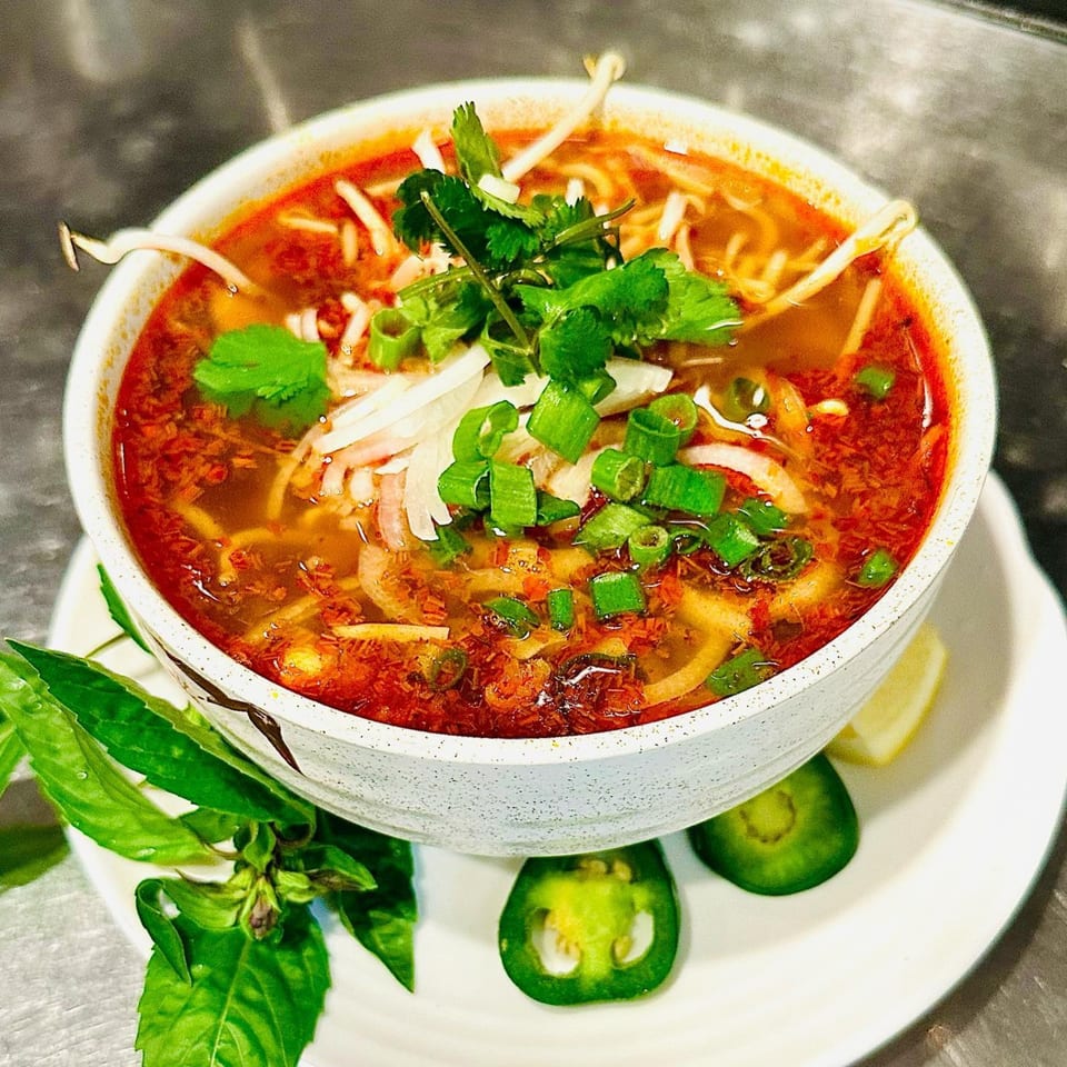 Spicy vegan noodle soup with bean sprouts, cilantro, and green onions, served with basil and jalapeños.